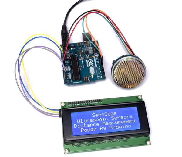 Arduino setup with ultrasonic sensor module connected to a blue LCD screen displaying SensComp distance measurement text.