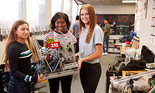 Three high school students holding a VEX robotics project in a classroom