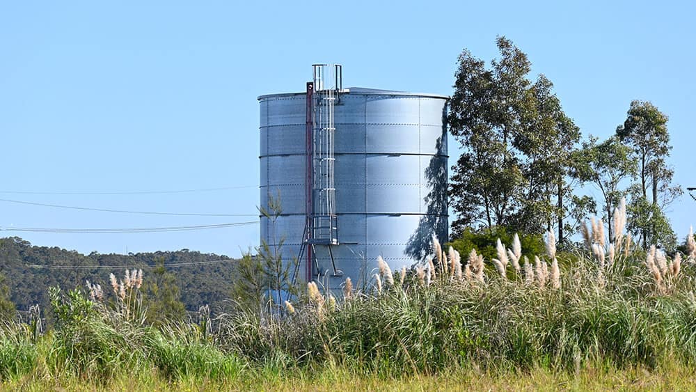 Galvanized water storage tank in an open field, where electrostatic ultrasonic transducers measure liquid level.