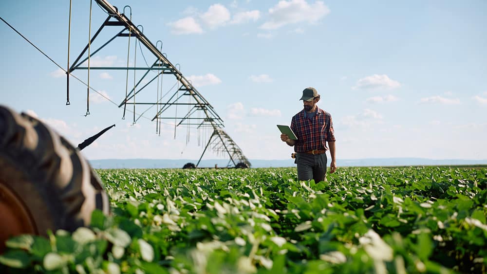 Grower with a tablet beside a center-pivot irrigation system supported by electrostatic ultrasonic level monitoring.